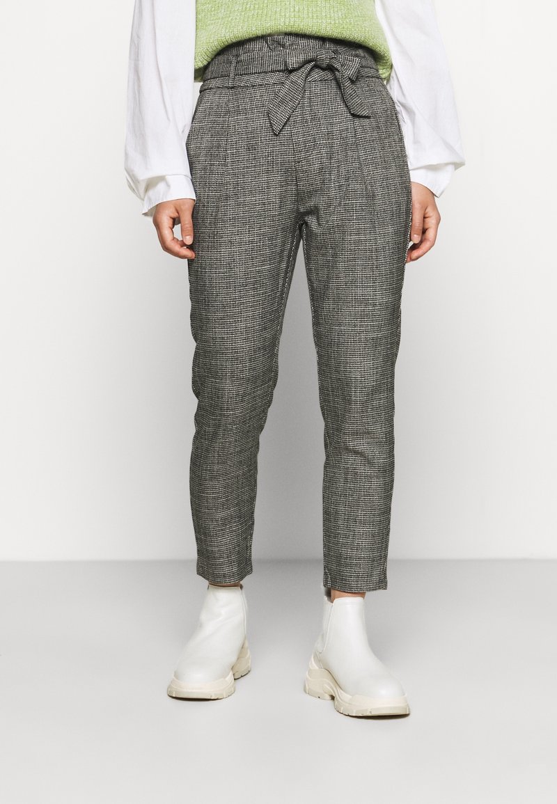 Grå rutiga byxor med bälte i midjan och veck, stylade med en vit skjorta och vita ankelstövlar. Slät textur och skräddarsydd passform.