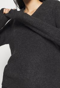 Maglione grigio scuro lavorato a maglia con scollo a V, maniche lunghe che superano il polso e una finitura del tessuto testurizzata.