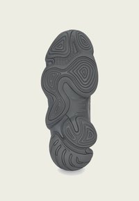 Sola de ténis de borracha preta com padrões e ranhuras intrincados, apresentando uma textura que não deixa marcas. Acabamento suave com contornos flexíveis.