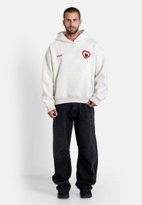 Witte oversized hoodie met een rood hartlogo op de borst, gecombineerd met zwarte baggy jeans. Bevat een voorkeurszak en ribgebreide manchetten.