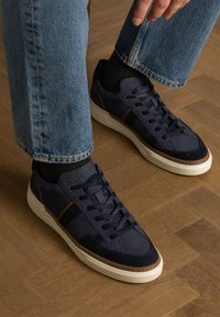 Sneakers blu navy con un mix di materiali lisci e testurizzati, con dettagli marroni, suola bianca e un classico design con lacci.