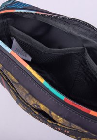 Černá tkaninová taška s živým vzorovaným exteriérem. Obsahuje zipové uzavření, hladký interiér a síťovou kapsu pro organizaci.