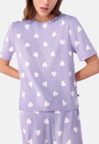 Lila shirt met korte mouwen en een ronde halslijn, versierd met witte hartpatronen. Gemaakt van een zachte, lichte stof met een relaxte pasvorm.