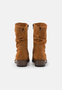 Bottes de cheville en suède marron avec un design décontracté, fermeture éclair et un talon en bois empilé. Détails de couture notables le long du bord supérieur.