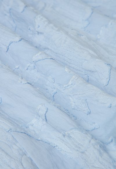 Helles blaues Gewebe mit strukturiertem Stickmuster. Weiches, leichtes Material faltet sich und offenbart filigrane Stickdetails in unterschiedlichen Farbtönen.