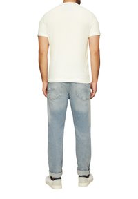 Witte korte mouwen t-shirt gecombineerd met lichtblauwe vervaagde jeans; casual pasvorm met achterzakken en opgerolde broekspijpen, gedragen met witte sneakers.