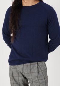 Pull en maille bleu marine avec un col rond et des manches longues, associé à un pantalon à carreaux gris. Texture douce et coupe ajustée.
