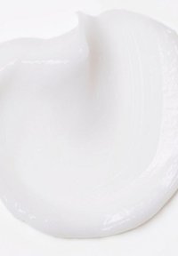 Witte crème met een gladde, glanzende textuur, iets dik, in een abstracte vorm gewerveld tegen een lichte achtergrond.