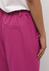 Fuchsia byxor med elastisk midja som har en sidoficka, slät textur och skräddarsydd passform designad för komfort och rörelsefrihet.