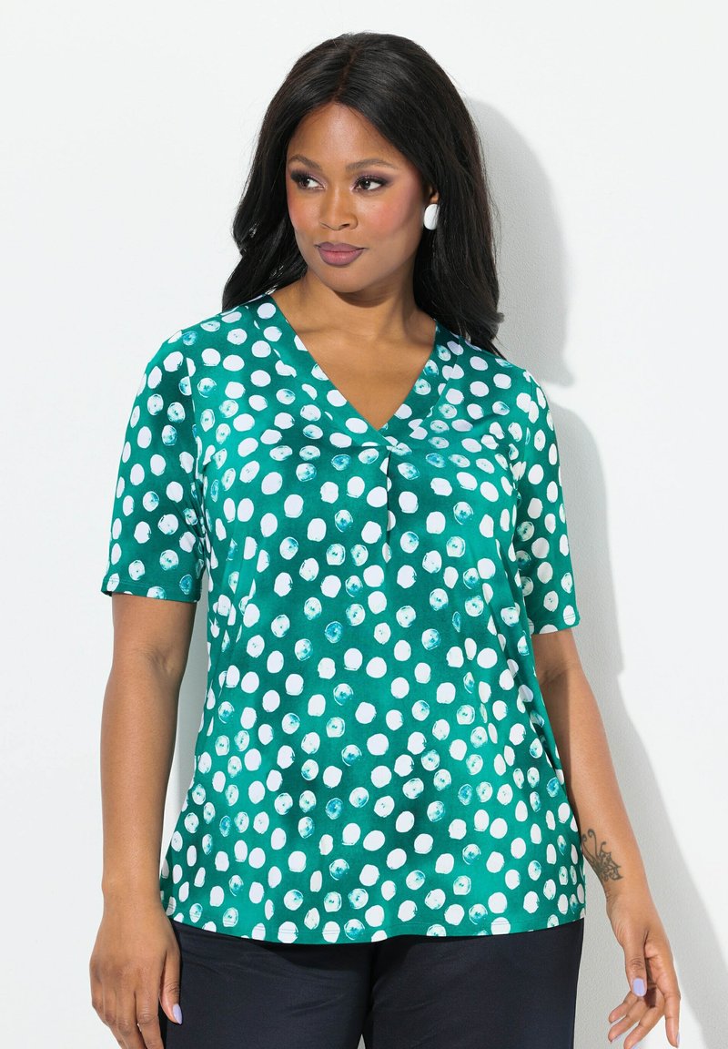 Teal blouse met korte mouwen, met een V-halsontwerp en een patroon van witte en blauwe stippen. Glad, lichtgewicht stof.
