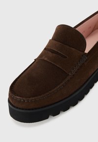 Pruun nahast loafers, millel on õmmeldud muster, kõrge pennikoht ja paks must kummitald. Silmapaistev tekstuur koos klassikalise kuju ja stiiliga.