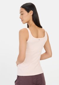 Light pink tank top featuring a scoop neckline, shoulder straps, and a tag on the back; smooth texture and fitted design.