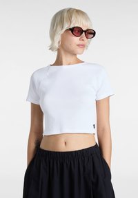 Top corto blanco acanalado con cuello redondo y mangas cortas raglán, combinado con pantalones negros holgados con una cintura elástica.