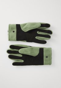 Pár zöld és fekete polárkesztyű, tapintásos tenyérrel és patentos záródással, síkban fektetve, fehér háttér előtt.