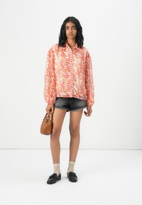 Floral-patterned, long-sleeved pink blouse with button closure, paired with denim shorts, black loafers, and a small brown handbag.