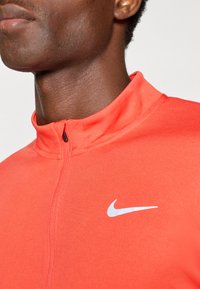 Red athletic zip-up jacket featuring a high collar and white Nike logo. Made of smooth, flexible fabric with visible stitching details.