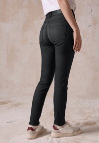 Svarta skinny jeans med bakfickor, en slät yta och midjehög passform. Kläderna kompletteras med vita sneakers med röda detaljer.