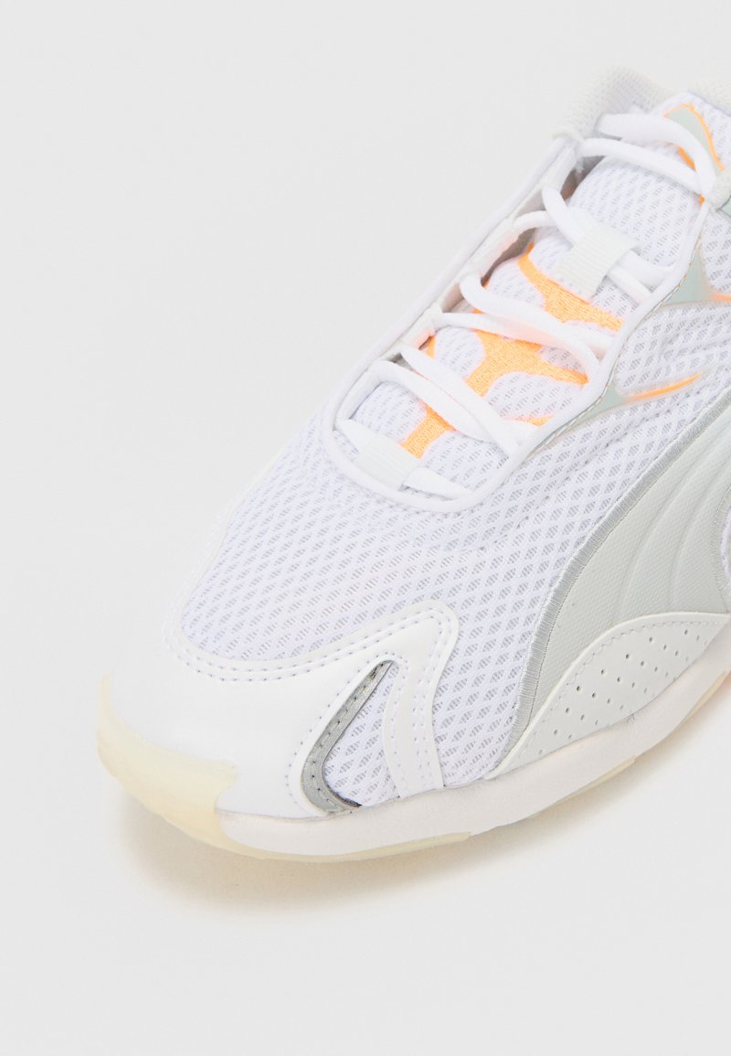 Baskets de sport blanches avec une tige en mesh, des accents texturés, des détails orange sur la languette et une semelle en caoutchouc flexible.