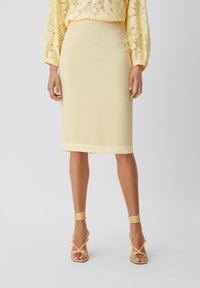 Knälång gul blyertkjol med en mjuk textur och fålldekor, i kombination med gul klackiga sandaler med remmar.