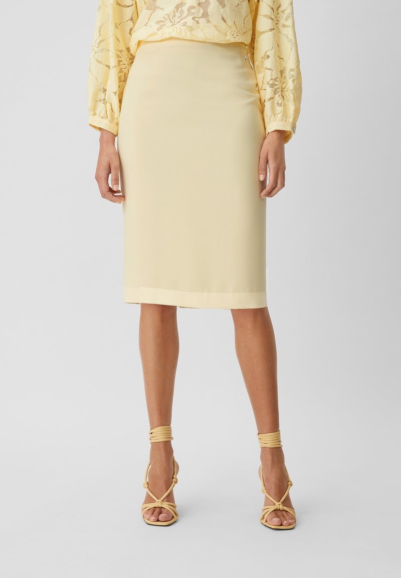 Knälång gul blyertkjol med en mjuk textur och fålldekor, i kombination med gul klackiga sandaler med remmar.