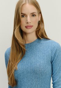 Maglione blu lavorato a maglia con scollo rotondo, caratterizzato da un motivo testurizzato. Maniche lunghe e un tessuto morbido e leggero completano il design.