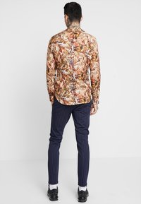 Košile na knoflíky s barevným a složitým vzorem na světlém pozadí, v kombinaci s námořnickými pruhovanými kalhotami a černými botami.