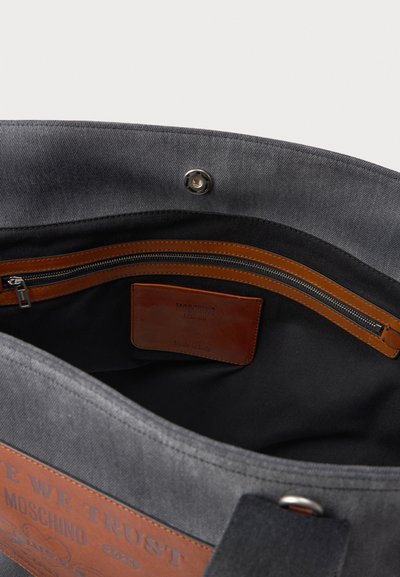 Γκρί καμβά τσάντα tote με δερμάτιν�ες λεπτομέρειες, διαθέτει τσέπη με φερμουάρ και ανάγλυφο λογότυπο. Ο εσωτερικός χώρος δείχνει λεπτομέρειες επένδυσης και υγρού.