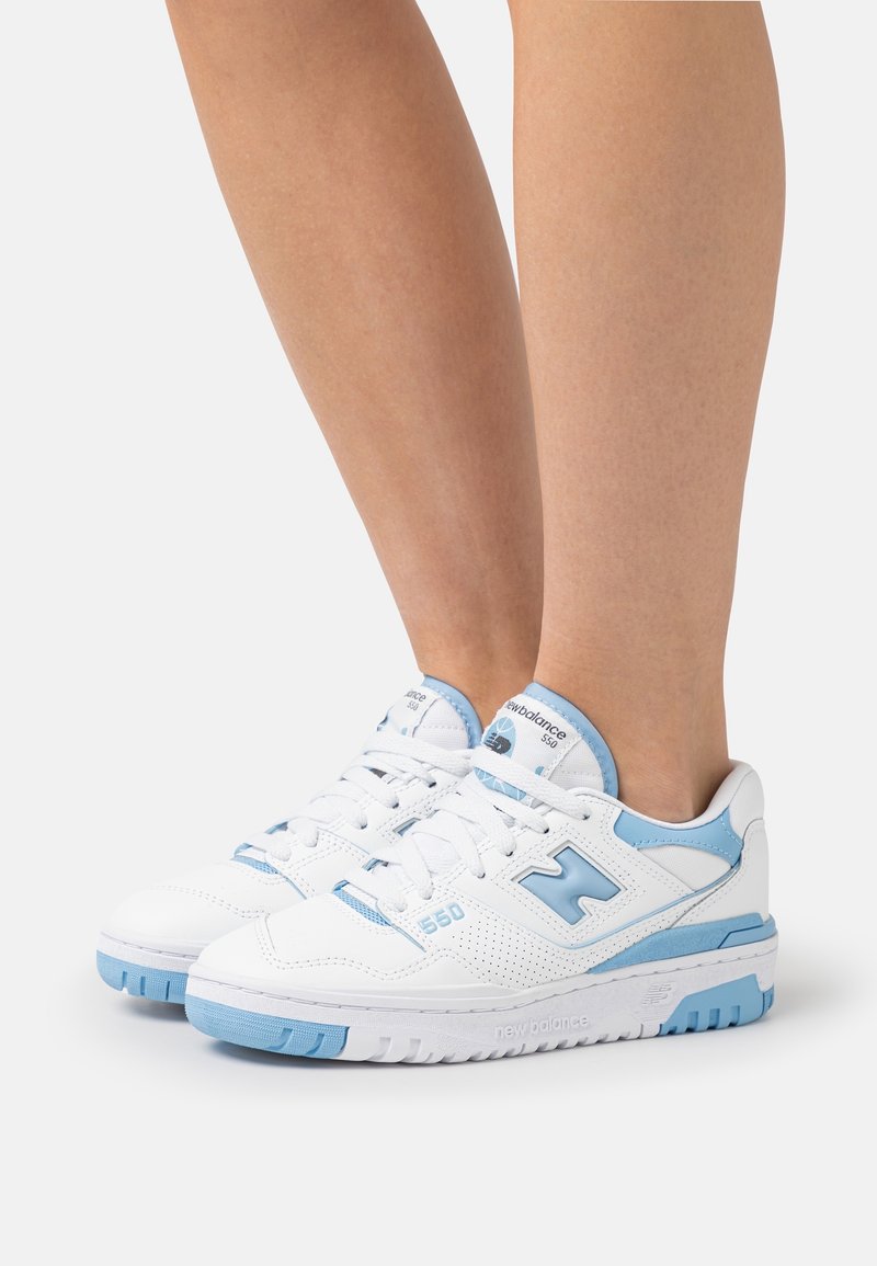 Weiße Sportschuhe mit hellblauen Akzenten, ausgestattet mit einem strukturierten Leder-Obermaterial, Schnürverschluss und einer dicken Gummisohle mit Branding.