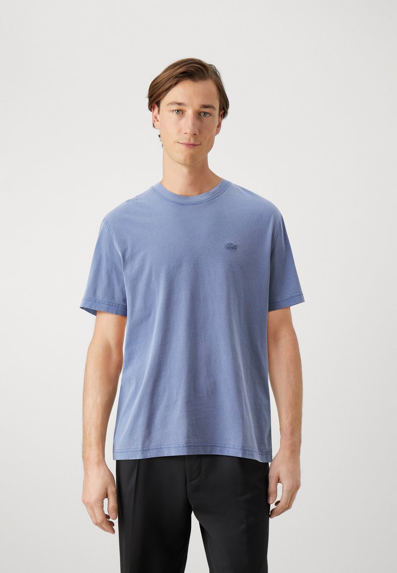 Camiseta de algodón azul de manga corta, con cuello redondo y un sutil detalle del logo en el lado izquierdo del pecho. Textura suave, corte relajado.