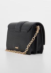 Borsa a mano in pelle nera con superficie testurizzata, design a patta piegata e tracolla a catena dorata. Presenta marchio in oro sul davanti.