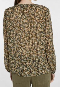 Blusa floral de tejido transparente, con un fondo marrón y pequeños flores rosas, azules y verdes. Mangas largas con puños fruncidos.