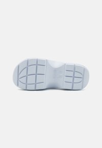 Suola di scarpa bianca in gomma con superficie texturizzata, dotata di grip, scanalature di flessione e forma della punta arrotondata, progettata per offrire trazione e comfort.