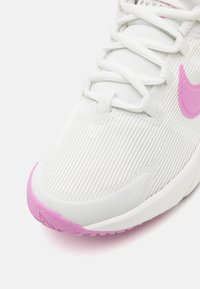 Baskets blanches de sport avec des rayures texturées, présentant un logo rose et des accents de semelle. Design à lacets avec un embout en caoutchouc contrastant.