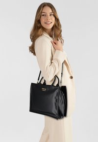 Borsa nera lucida realizzata in materiale liscio, con manici doppi, una forma strutturata e un logo dorato sul davanti.