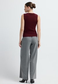 Top sin mangas en burdeos combinado con pantalones de pierna ancha en gris; los zapatos son negros con punteras afiladas. Tejido de punto suave; sin dibujos ni patrones.