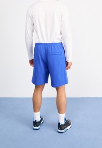 Niebieskie bawełniane szorty z elastycznym pasem i bocznymi kieszeniami, w połączeniu z białymi długimi rękawami oraz czarnymi butami sportowymi z niebieskimi akcentami.