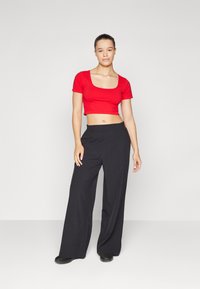 Top corto rosso con maniche corte, abbinato a pantaloni neri larghi. L'outfit presenta un design semplice con scollatura rotonda.