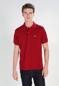 Red polo shirt in cotton fabric, featuring a collar, short sleeves, and a green Lacoste crocodile logo on the left chest.