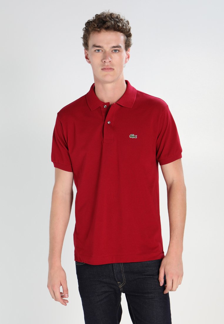 Red polo shirt in cotton fabric, featuring a collar, short sleeves, and a green Lacoste crocodile logo on the left chest.