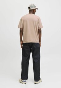 Beige katoenen t-shirt met korte mouwen, gecombineerd met donkerblauwe spijkerbroek en beige sneakers met een grijze en bruine pet.