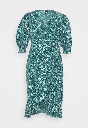 Teal wikkeljurk met witte onregelmatige stippen, pofmouwen met geplooide manchetten en ruches langs de zoom en de vooroverlapping.