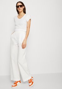T-shirt en coton blanc à manches courtes, associé à un pantalon blanc ample avec une ceinture élastique, et des baskets orange et blanches.