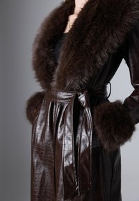 Cappotto in finta pelle marrone con motivo a coccodrillo, dotato di un ampio colletto e polsini in pelliccia, legato in vita con una cintura coordinata.
