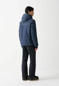 Námořnická puffer bunda s kapucí, která má prošívané akcentové pruhy. V kombinaci s černými soft-shell kalhotami a tmavou obuví se světlou podrážkou.