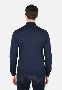 Maglione lavorato a maglia blu navy con colletto alto, maniche lunghe e polsini e orlo a costine. La trama del tessuto appare liscia con un design aderente.