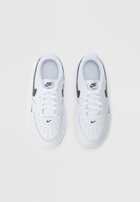 Paru bijelih tenisica Nike Air Force 1 s crnim Swoosh logotipima i perforiranim prednjim dijelom, prikazanih odozgo na bijeloj pozadini.