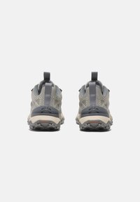Zapatos de senderismo grises y beige con parte superior de malla, suela de goma texturizada y lengüetas en el talón para ponerlos y quitarlos fácilmente. Diseñados para la durabilidad y la tracción.