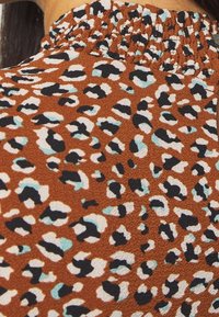 Brun tyg med smockad halsringning, med ett leopardmönster i svart, vitt och ljusblå accenter. Strukturerad, avslappnad stil.