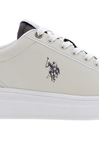 Krämfärgade lädersneakers med vit gummisula, med en svart polo-spelare logo på sidan och vita snören som fäster ovandelen.