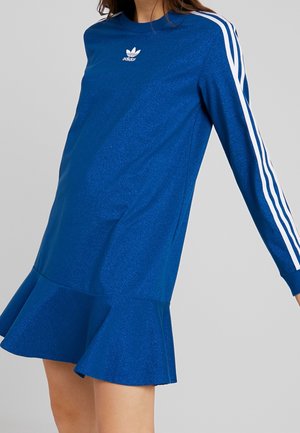 Modré šaty s dlouhým rukávem s bílým logem Adidas na hrudi a třemi bílými pruhy na rukávech, které má na sobě osoba na šedém pozadí.